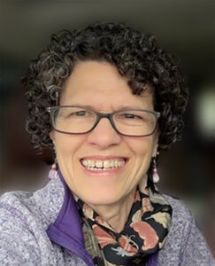 Woman with curly hair and glasses, smiling at the camera